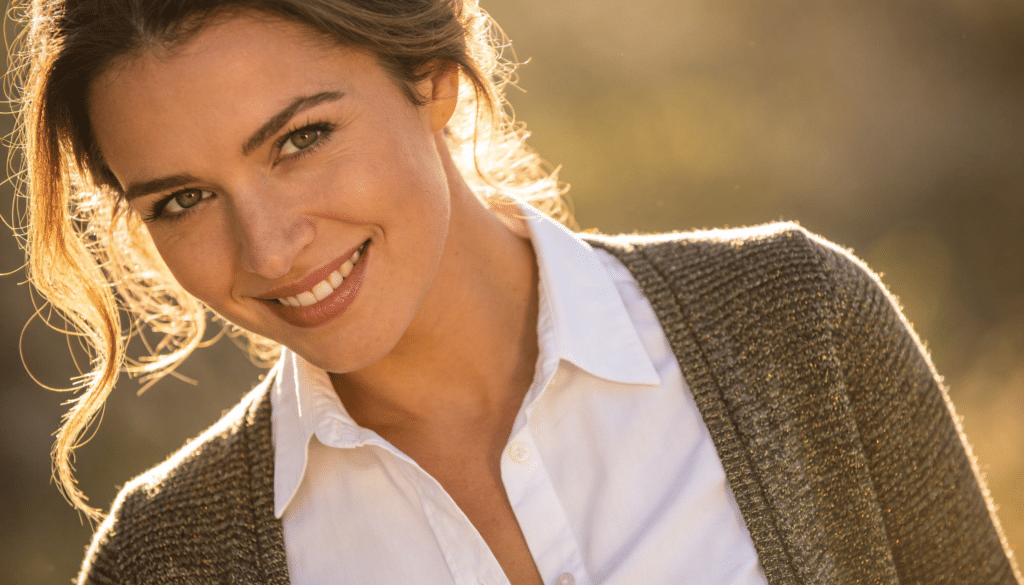 femme séduisante de 30 ans portant cardigan fin et chemise blanche, sourire naturel, lumière douce matin